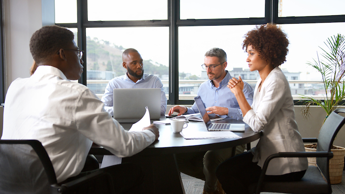 Multi-Cultural Business Team Meeting Collaborating Sitting Around Table In Modern Office Together